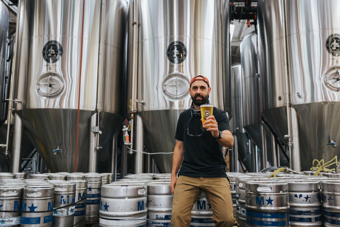 Picture of Coronado Brewing Co. Head Brewer holding beer in front of fermentation tanks